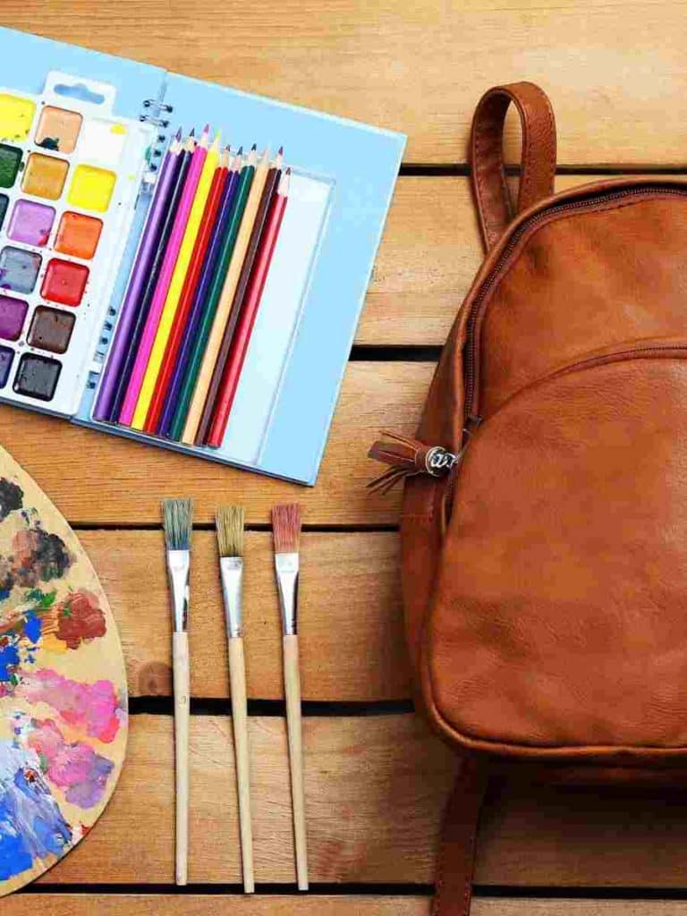 a brown backpack next to a set of watercolor paints and paint brushes